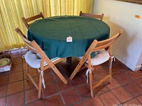 Round pedestal table covered with green tablecloth and 4 wooden folding chairs with padded cushions placed around it on tile floor