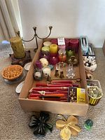 Overview of candles including large green candle with turtle decor and wooden holder, various pillar candles, red taper candles, brass candle holder, small pie candle with glass holder, and shamrock paperweights.