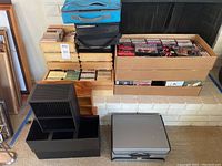 Overview of whole lot showing boxes full of cassettes and CDs stacked on and near a white brick hearth. Two blue and black music case organizers and additional black storage cases on floor.