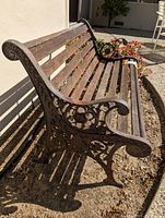 Side angle showing wooden slats and ornate cast iron armrest with floral scrollwork detail.