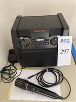 Front view of the ION Sport Go portable PA speaker with control panel and microphone placed in front, showing included wired connection.