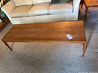 Top view of mid century teak wood coffee table showing wood grain, scratches, and tag.