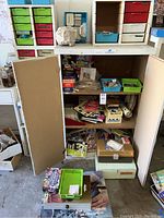 White storage cabinet with colored plastic drawers, open lower doors revealing books, specimen trays and boxes
