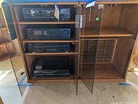 Wooden cabinet with glass doors containing four audio components arranged on shelves: Pioneer dual-deck cassette player, Pioneer SX-1300 stereo receiver, TEAC PD-D860 compact disc player, and Technics SL-BO22 record player at bottom.