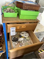 Wooden six-drawer chest with drawers partially open showing seashells inside and green plastic trays on top with stones and shells.