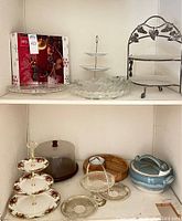 Shelf display showing multiple serving and display dishes including Mikasa platter, floral patterned bowls, tiered serving plates, domed cake saver, wood chip & dip bowl, two-handled ceramic bowl.
