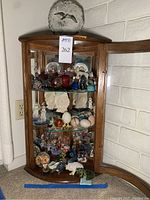 Full view of wooden display cabinet with open glass door showing multiple decorative items arranged on three shelves.