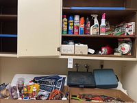 Shelf with assorted household cleaners, insecticide sprays, First Alert alarms, and tool cases below the shelf, plus hand tools in boxes and cases on the counter.