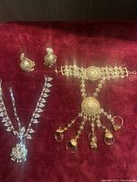 Gold-tone ornate bracelet with hanging charms, matching earrings, and silver-tone necklace on red velvet background.