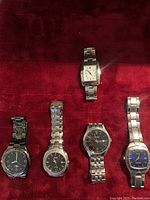 Five men's wristwatches displayed on red fabric surface showing front views including face and bands