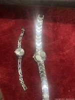 Two women's wrist watches laid on a red surface, one smaller with silver-tone linked oval band and the other larger with two-tone metal band.