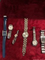 Six women's wrist watches arranged on a red velvet surface showing different band materials and watch face shapes and colors.