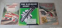 Three vintage railroad books displayed side by side on a surface, titles visible: Rails Across America, The Railroad Story, Clear the Track.