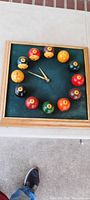 Square clock in solid oak frame with outer dimensions about 14x14 inches. Clock face features 12 real billiard balls corresponding to hours. Clock hands visible at 10:10.