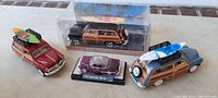 Four diecast vehicles including three surfboard station wagons and a smaller 1954 Chevrolet custom car model, all approximately 6 inches long.