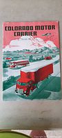 Magazine cover with trucks illustrated in red and green, airplane flying, and mountains in background.