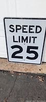 Photo showing the front of the rectangular metal street sign with black text 'SPEED LIMIT 25' on white background. Normal surface wear visible.