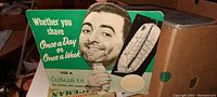Photo showing the front of the vintage cardboard easel sign with a man's face, razor image, and promotional text about shaving.