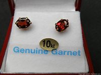 Close-up of the oval garnet stones set in 10k gold prongs inside a jewelry box showing the 10kt gold label and 'Genuine Garnet' text on backing paper.