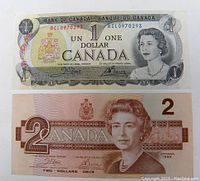 Front of 1 dollar 1973 and 2 dollar 1986 Canadian banknotes showing Queen Elizabeth II and denomination details.