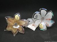 Two Murano glass flowers viewed from above showing labels and colorful swirl designs.