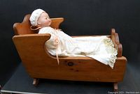 Side view of the Armand Marseille doll in wooden cradle, showing full length and detailed lace gown