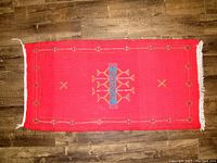 Full view of the rectangualr red Moroccan carpet with geometric embroidered patterns and white fringes on the edges.