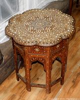 Front-angle view of antique wooden table showing scalloped top with detailed mother-of-pearl inlay.