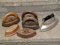 Six antique sad irons displayed on steps, showing different handle types and iron bases.