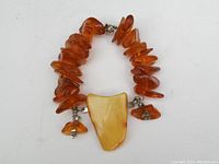 Full view of amber-like Beads in bracelet with large central amber-colored pendant and metal clasp.