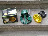 Items shown include the Yard Master outdoor floodlight kit box with floodlight, a green extension cord with a ground stake plug, and an additional outdoor floodlight.