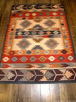 Full view of vintage Kilim style carpet with geometric diamond and arrow motifs in a mix of red, blue, beige, and brown hues.