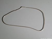 Photo showing full length of thin sterling silver chain necklace laid flat on a grey surface.