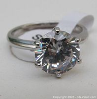 Close-up front view of sterling silver ring with large clear round faceted gemstone held by six prongs.