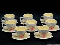 Front angled view of 8 tea/coffee cups arranged with their matching saucers. Shows honeycomb textured cups with pink rose floral pattern and cream-colored saucers with triangular shape.
