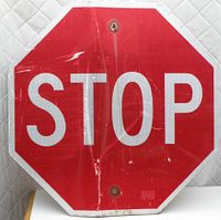 Front of the vintage red octagonal stop sign showing the word 'STOP' in white letters with dents and scratches visible.