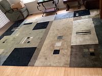Full view of the large rectangular area rug on light wood floor with abstract blocks and squares in earth tones.