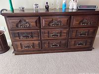Full front view of dark wood dresser showing 9 drawers with decorative metal pulls.