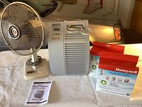 Photo showing Honeywell air purifier, Sanyo fan, two red-topped Honeywell filter boxes, and manuals on a table.