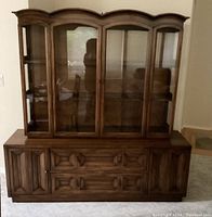 Front view of two-piece walnut hutch display cabinet with glass doors upper section and wooden paneled doors and drawers lower section.