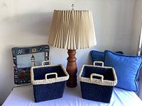 Photo shows entire lot: wooden lamp with beige pleated shade, two navy and beige jute baskets, and three blue pillows including beach-themed one with lighthouse design.