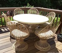 Full view of round patio table with six woven fiberglass dining chairs on deck