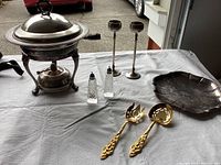 Entire lot setup including filigree plated utensils, candlestick holders, small platter, warming stand with serving dish and glass salt and pepper shakers.