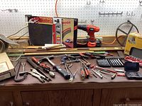 Full view of assorted small hand tools spread out on table with Black & Decker drill, wooden folding rulers, boxed Router Edge Guide, tool bit sets, and various hand tools.