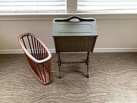Front view of the vintage mini sewing table side by side with the wooden magazine holder on carpeted floor near window.