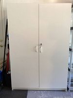 Closed front view of one white storage cabinet showing double doors and metal handles