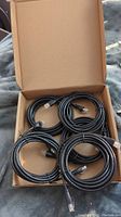 Five black Ethernet cables coiled and placed inside an open cardboard box, showing the RJ45 connectors clearly.