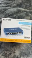 Front box image showing Netgear Business 8-Port Gigabit Ethernet Unmanaged Switch labeling, product image, and key features.
