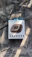 Box of Anker conference speakerphone displayed on a fabric surface showing product name and image on front.