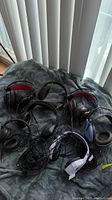 Photo of six wired headphones assorted on a grey blanket including black, black with red accents, and black with blue accents.